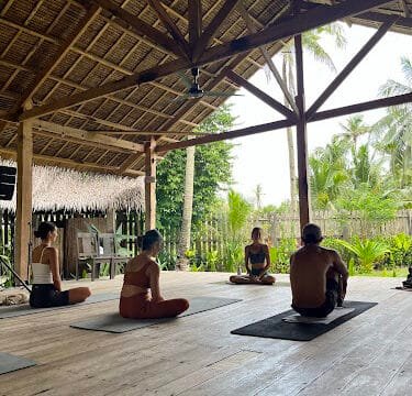 People sitting on yoga mats in an open-air wooden pavilion surrounded by Siargao’s lush trees and tropical greenery.