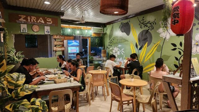 People dining inside a cozy, plant-themed Siargao restaurant with green walls and a red lantern hanging by the entrance.