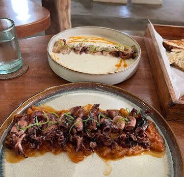 A plate of grilled octopus on sauce with herbs, and a dish of creamy dip with bread, served on a wooden table in Siargao.