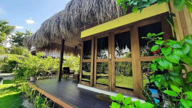 A tropical Siargao bungalow with a thatched roof, wooden deck, and lush green plants surrounding the porch.