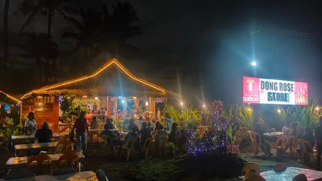 Outdoor restaurant at night in Siargao with people dining, string lights, tropical plants, and a bright Dong Rose Store sign.
