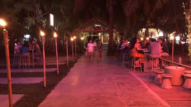Outdoor restaurant at night in Siargao, with tiki torches lighting the path, palm trees, and people dining at tables.