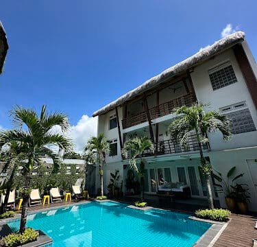 A clear blue pool in Siargao, surrounded by palm trees and a modern three-story building under a bright, sunny sky.