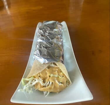 A Siargao-style wrapped sandwich or burrito filled with lettuce and sauce on a rectangular white plate.