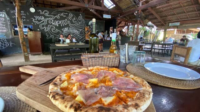 A wood-fired pizza topped with prosciutto served at a Siargao open-air restaurant with a chalkboard wall.