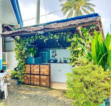 Outdoor kitchen with leafy plants, a bamboo cabinet, white countertop, and Siargao vibes from the palm tree in the background.