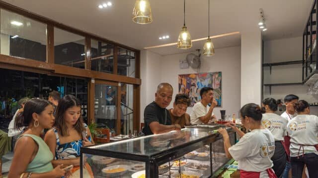 People choosing food at a busy counter inside a well-lit Siargao café, with staff serving behind the glass display.