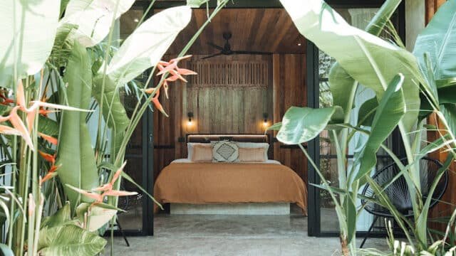 Cozy Siargao bedroom with wooden decor, orange bedding, and lush tropical plants in the foreground.