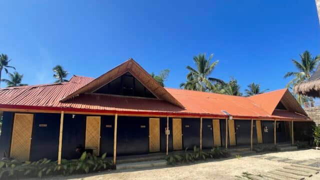 Single-story Siargao building with a red roof, blue walls, and palm trees in the background under a clear blue sky.