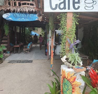 Outdoor cafe entrance in Siargao with plants, a sunflower mural, and a Cafe sign hanging above the walkway.