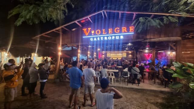 Crowd gathers outside Violegre Gastropub in Siargao at night, warmly lit with neon signs and rustic wooden décor.
