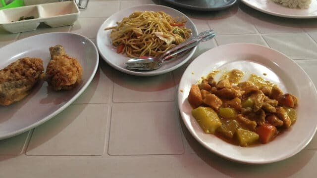 Plates of fried chicken, noodles, rice, soup, and Siargao-style chicken stew with vegetables on a table.