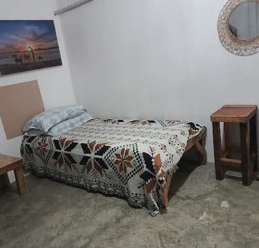 A simple Siargao bedroom with a single bed, patterned blanket, wooden furniture, wall art, and a round mirror.