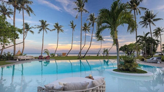 Tropical Siargao resort pool with palm trees, lounge chairs, and an ocean view at sunset.