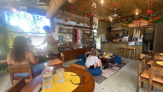 Cozy Siargao café with people seated at tables and floor cushions, a barista, and casual, rustic interior decor.