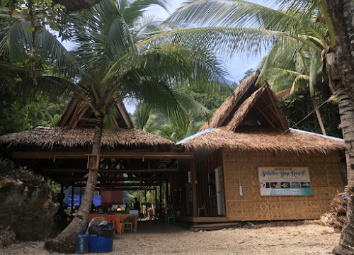 A tropical Siargao beach hut with thatched roofs and palm trees, with tables and chairs set up outside.