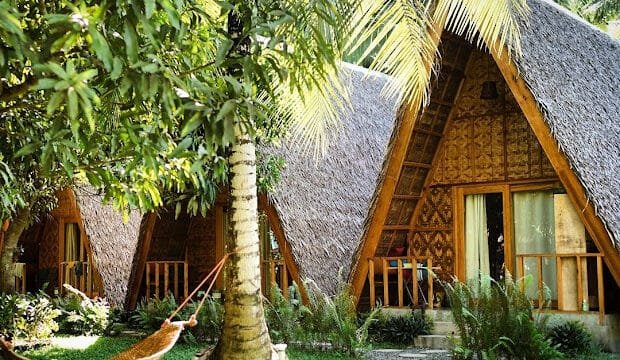 Three thatched A-frame huts with porches, a hammock tied to a tree, and lush Siargao tropical greenery all around.
