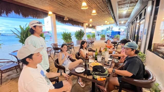 A group of people sit around a table at a Siargao beachside restaurant, eating and talking.