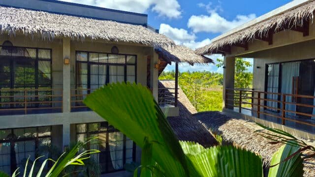 Tropical resort buildings with thatched roofs and large windows nestle amid green palm leaves in beautiful Siargao.