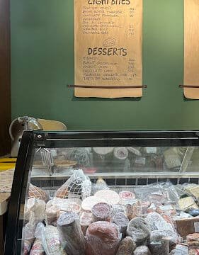 Deli counter with assorted meats and cheeses in Siargao, menu on wall listing light bites and desserts.