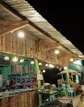Nighttime view of a rustic outdoor market stall in Siargao, with bright lights, empty chairs, and tables under a tin roof.