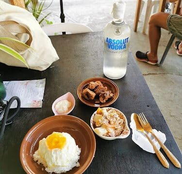 A table in Siargao with rice and egg, meat dishes, sauce, utensils, and a bottle of Absolut vodka.
