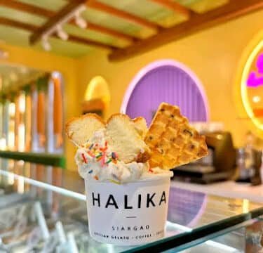 Cup of gelato with sprinkles, waffle, and bread slices on a glass counter in a colorful Siargao café.