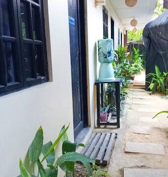 A narrow walkway in Siargao with potted plants, doors, and a blue water dispenser on a stand outside a building.