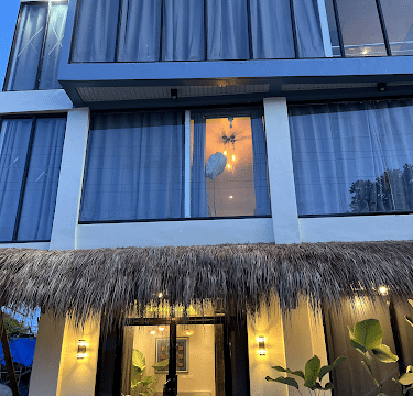 Modern three-story house with large windows, a thatched awning, and Siargao-inspired plants by the entrance at dusk.