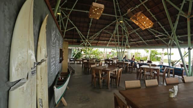 Open-air café in Siargao with wooden tables, surfboards on the wall, and a thatched roof, nestled near lush greenery and the sea.