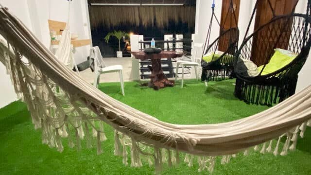 Siargao-inspired indoor patio featuring green artificial grass, a hammock, hanging chairs, and a table with chairs in the background.