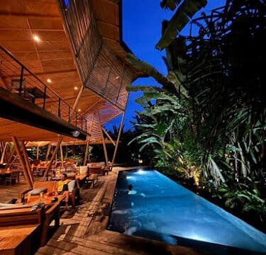 Modern outdoor restaurant at night in Siargao with a lit pool, wooden deck, and lush tropical plants.