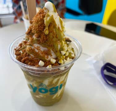 A cup of yogurt topped with cookie crumbs, white chocolate chips, and sauce on a table in Siargao.