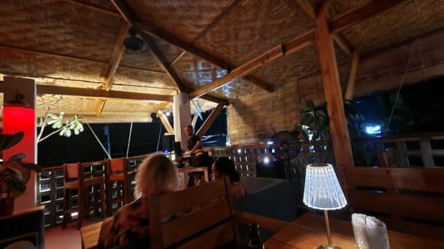 People sit at a cozy, dimly lit outdoor restaurant in Siargao with wooden decor and a thatched roof at night.