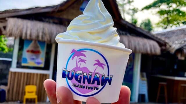 Hand holding a cup of soft-serve froyo in front of a thatched hut labeled Bugnaw Island Froyo on Siargao.