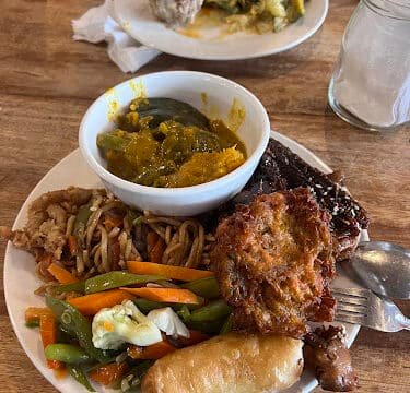 A plate of assorted food including noodles, vegetables, fried items, and a bowl of yellow curry on a wooden table in Siargao.