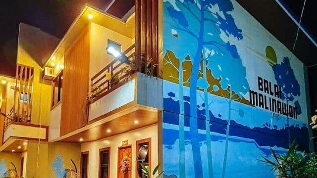 A brightly lit building at night in Siargao, featuring a large blue mural and the words Balai Malinawon on the wall.