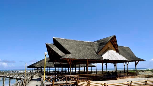 Wooden pier with thatched-roof pavilions over Siargao’s clear water under a bright blue sky.