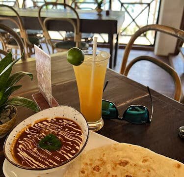 Bowl of beans with sauce, tortilla, and a glass of juice with lime on a sunny Siargao restaurant table.