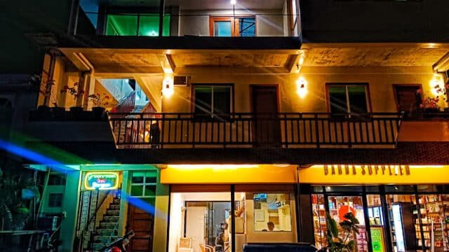 Three-story building at night in Siargao with lit windows, neon signs, and parked motorcycles out front.