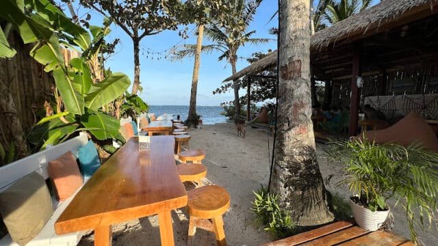 Outdoor beach café in Siargao with wooden tables, stools, palm trees, and ocean view under a clear blue sky.