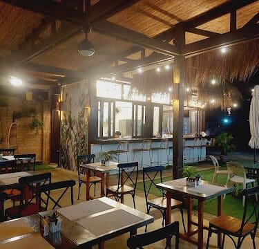 Outdoor restaurant seating area with wooden tables, chairs, and string lights, offering a cozy, rustic Siargao ambiance at night.