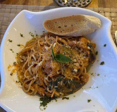 Spaghetti with tomato sauce, spinach, grated cheese, basil, and baguette served Siargao-style on a white plate.