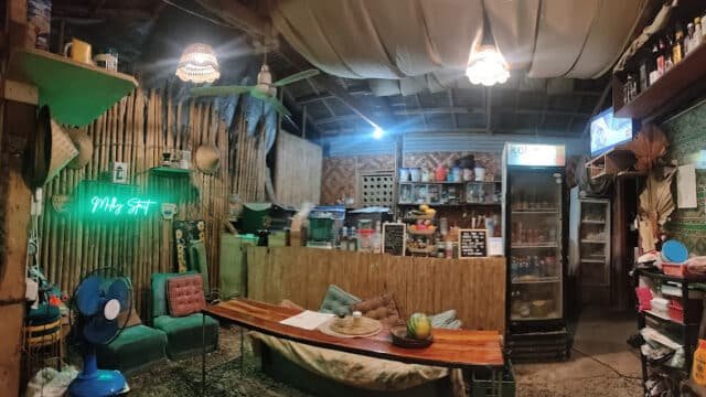 Cozy rustic café interior in Siargao with bamboo decor, sofas, wooden table, fridge, and neon Milk Set sign.