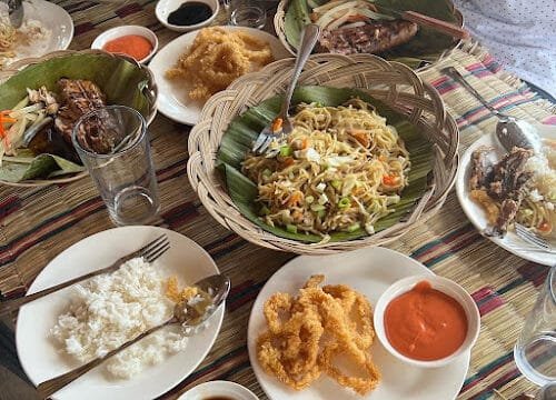 Table with rice, noodles, fried food, dipping sauces, and grilled meat on banana leaves—a true Siargao feast enjoyed together.