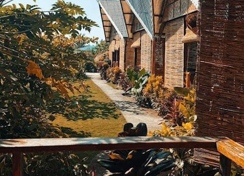Row of rustic villas with bamboo walls, lush green plants, and a sunlit garden path at Mera’s Garden in scenic Siargao.