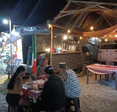 Four people dine at an outdoor food stall in Siargao at night, under glowing lights and a checkered tablecloth.