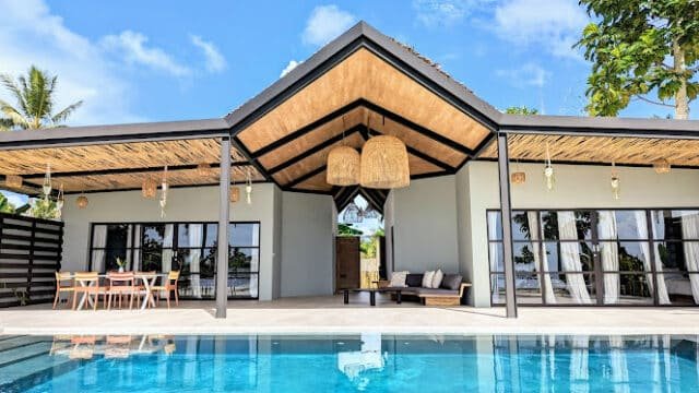 Modern Siargao villa with a pool, outdoor dining area, and glass doors under a clear blue sky.