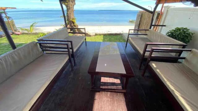 Outdoor wooden seating area under a canopy in Siargao, facing the sea with a clear, sunny view of the beach.