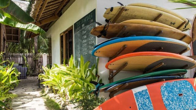 Six colorful surfboards are stacked outside a Siargao beach hut, surrounded by lush tropical plants.